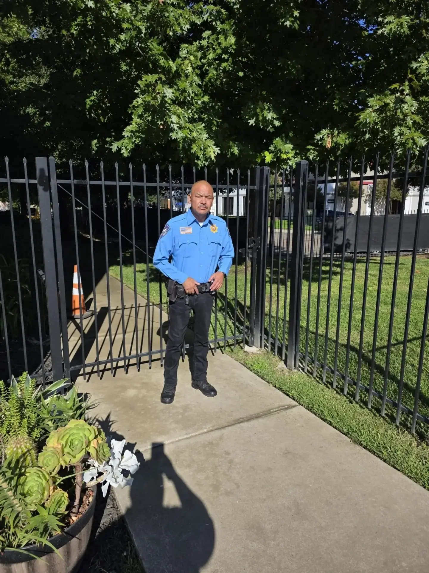 Security guard standing at an open gate near a grassy area with trees